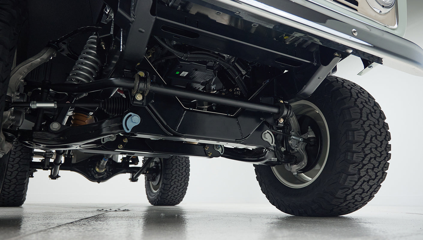 View of suspension, steering, and axle components from underneath Classic Ford Bronco with front left tire visible