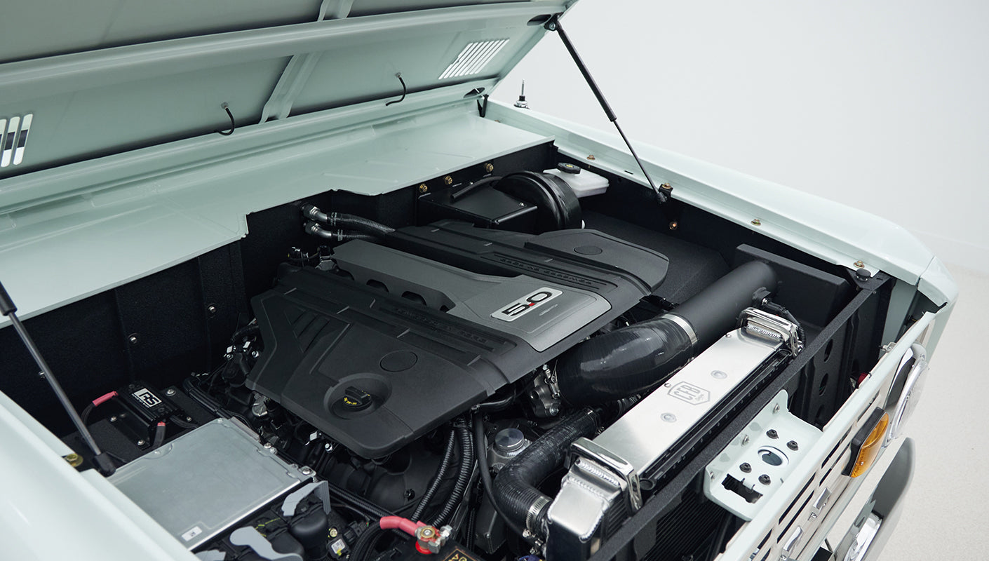 Clean engine bay of Classic Ford Bronco showing black engine cover labeled 5.0 with surrounding components