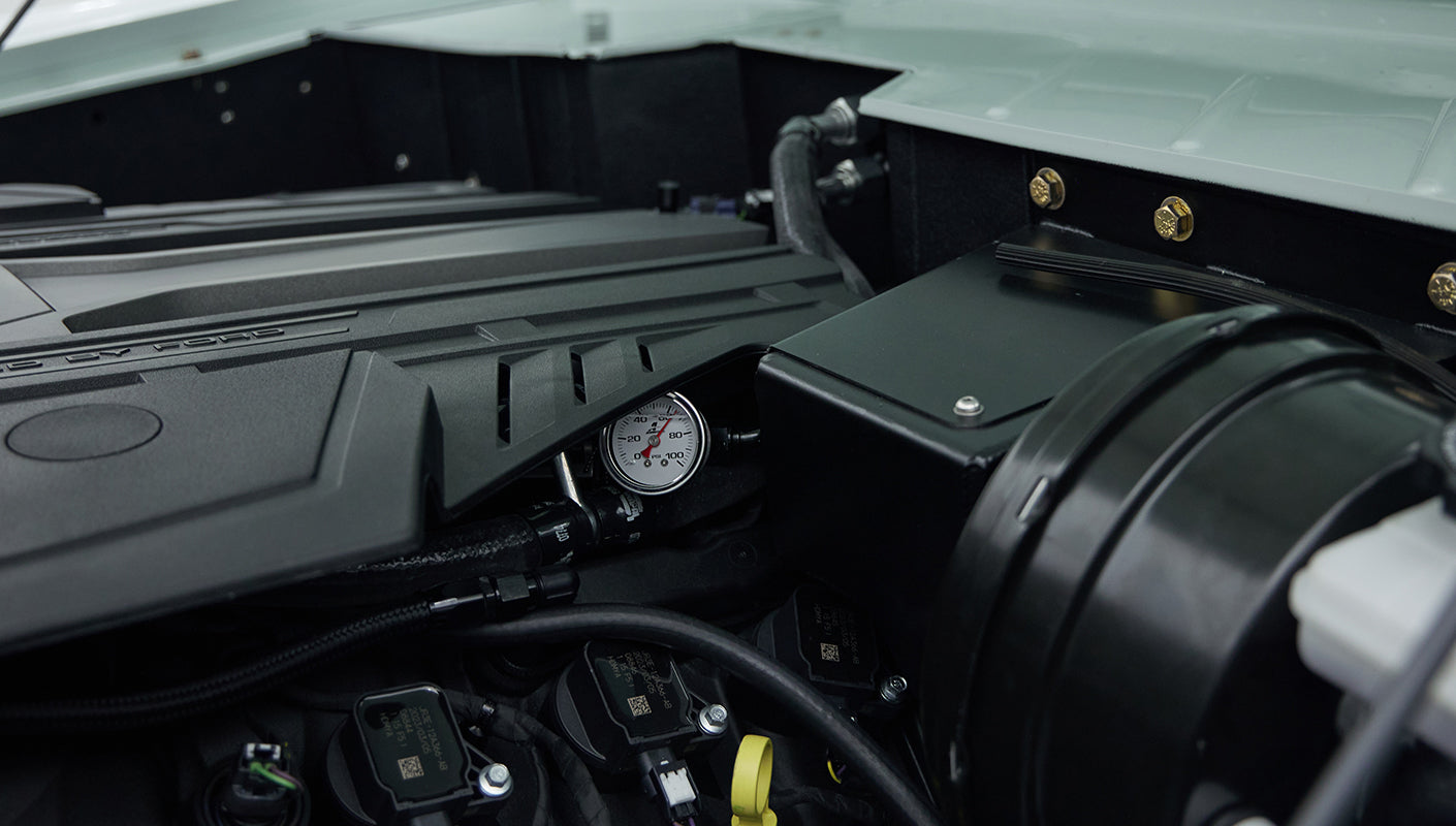 Close-up of engine bay featuring pressure gauge, hoses, and engine cover with 5.0 label
