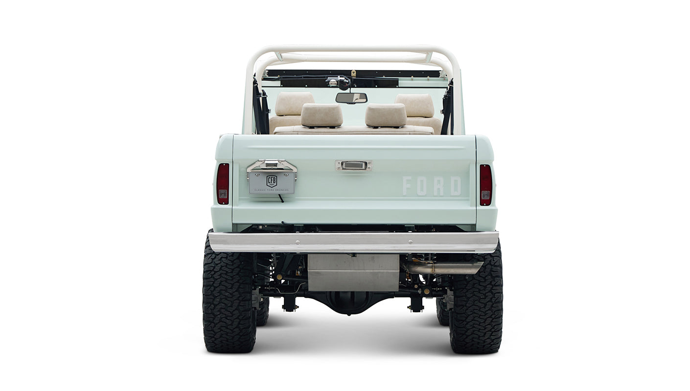 Rear view of a Classic Ford Bronco in pale blue with white roll cage and visible off-road tires.