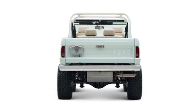 Rear view of a Classic Ford Bronco in pale blue with white roll cage and visible off-road tires.