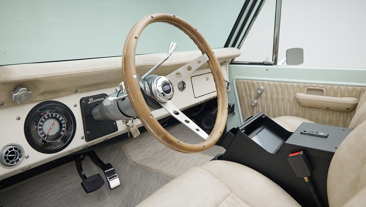 Classic Ford Bronco interior showing wooden steering wheel, dashboard, and beige seat with open center console