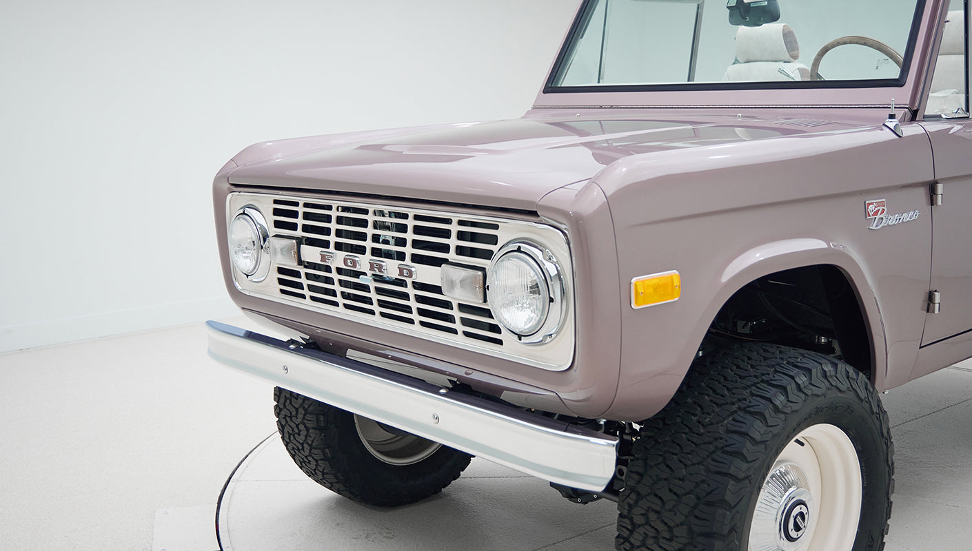 Close-up angled front view of Classic Ford Bronco with chrome grille, round headlights, and off-road tires