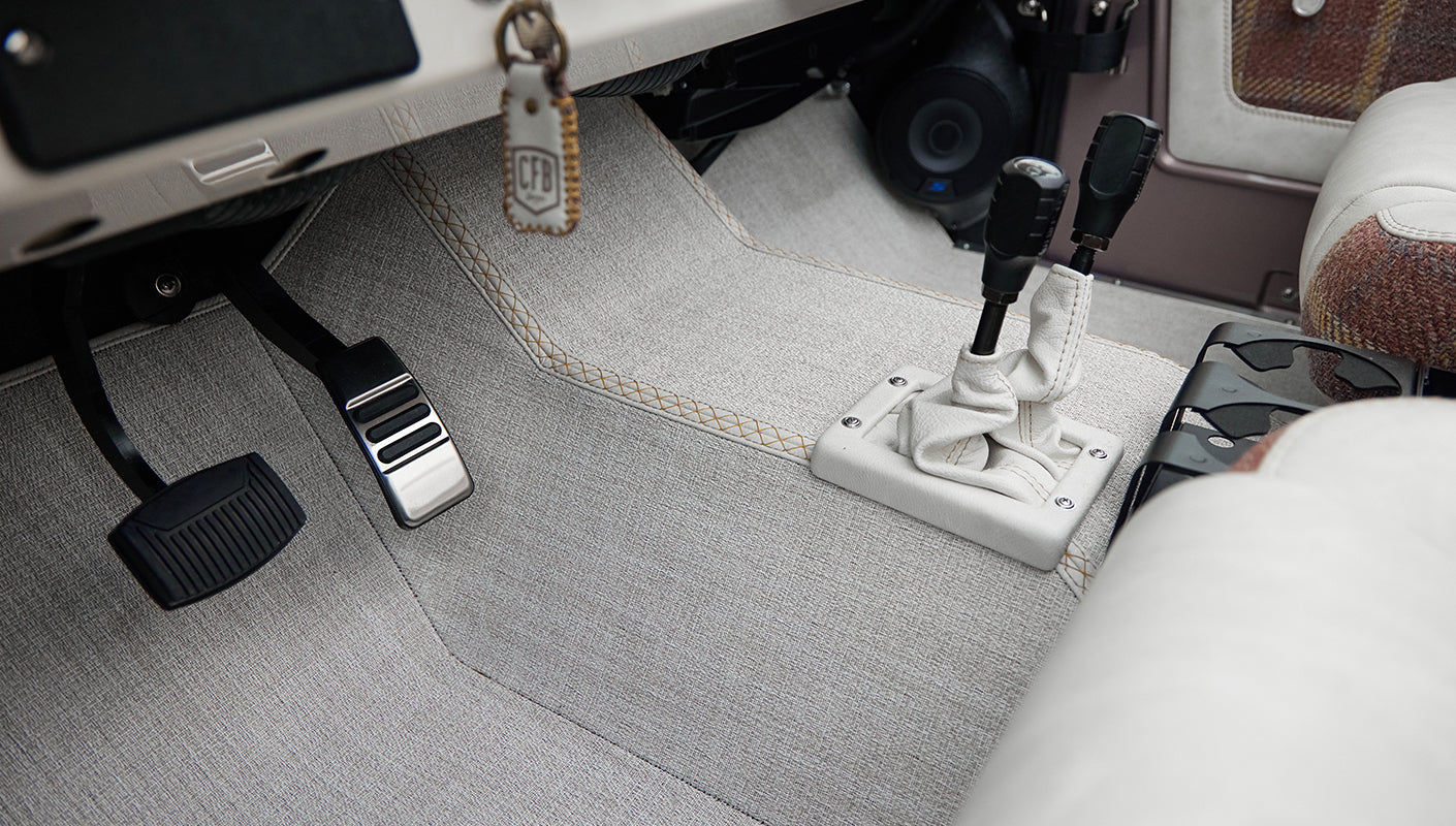 Classic Ford Bronco floor and pedals area with gray carpeting and dual gear shift levers wrapped in light material.