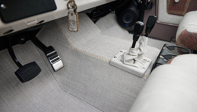 Classic Ford Bronco floor and pedals area with gray carpeting and dual gear shift levers wrapped in light material.