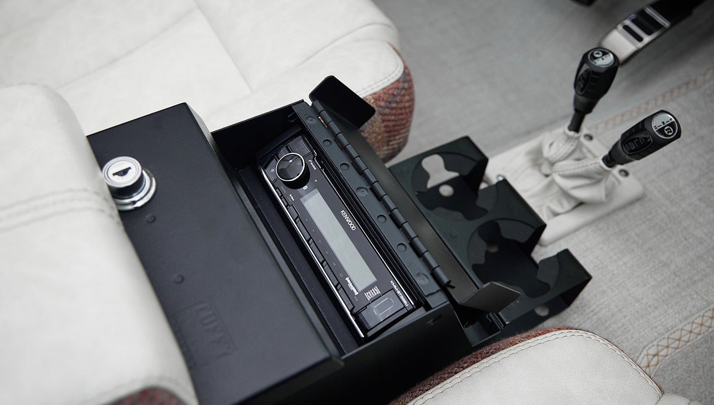 Center console of Classic Ford Bronco with open compartment housing a Kenwood stereo system and cup holders.