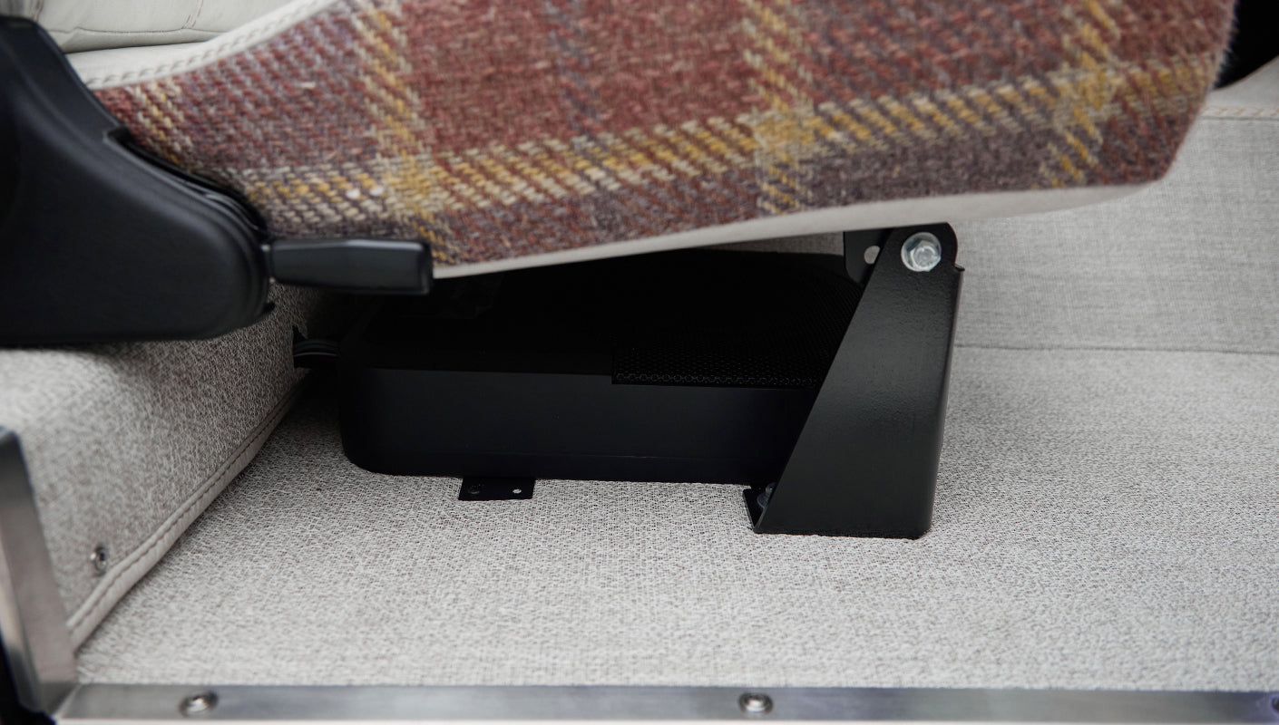 Black metal case or box mounted under a seat on a textured gray carpeted floor, Classic Ford Bronco interior.