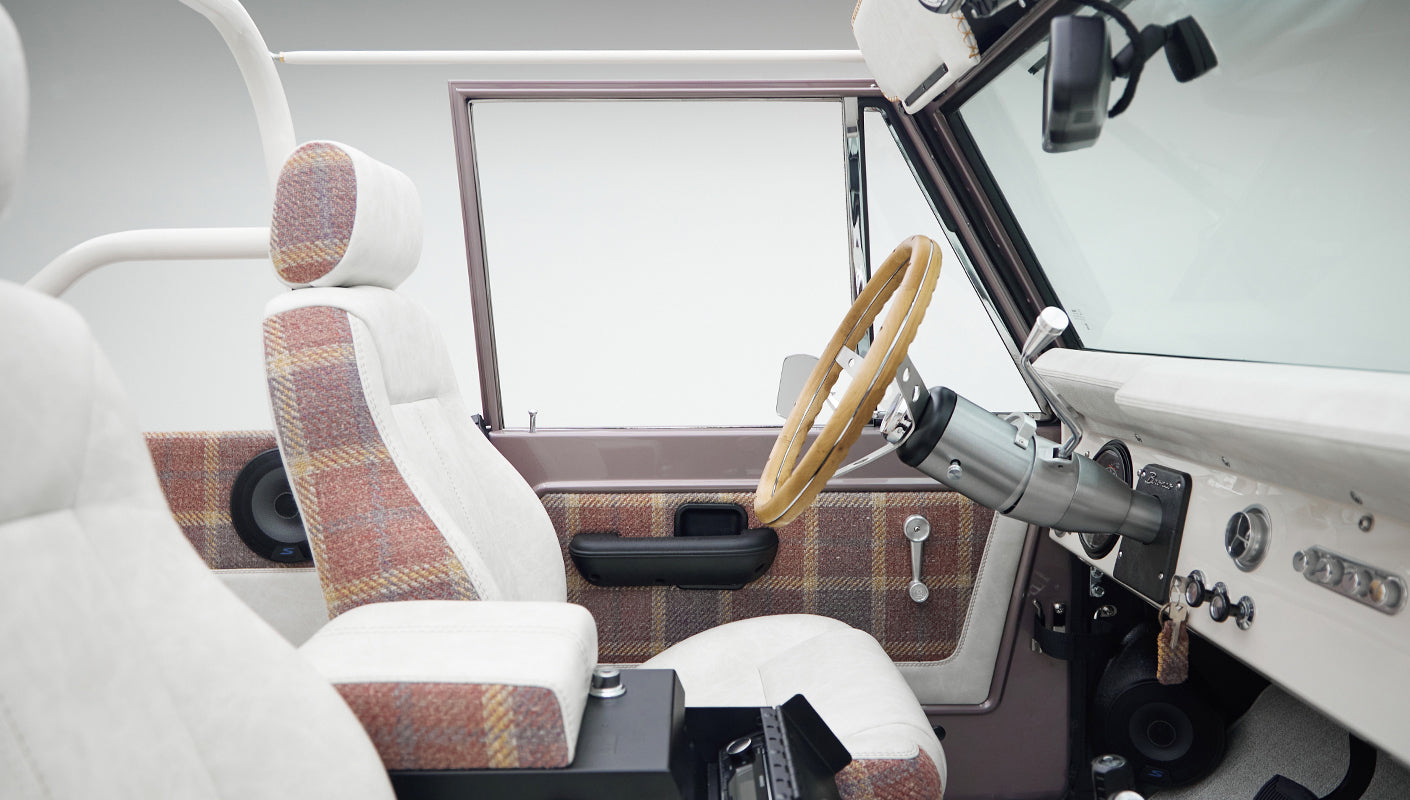 Interior side view of Classic Ford Bronco showing driver side door panel and front seats with plaid and white upholstery
