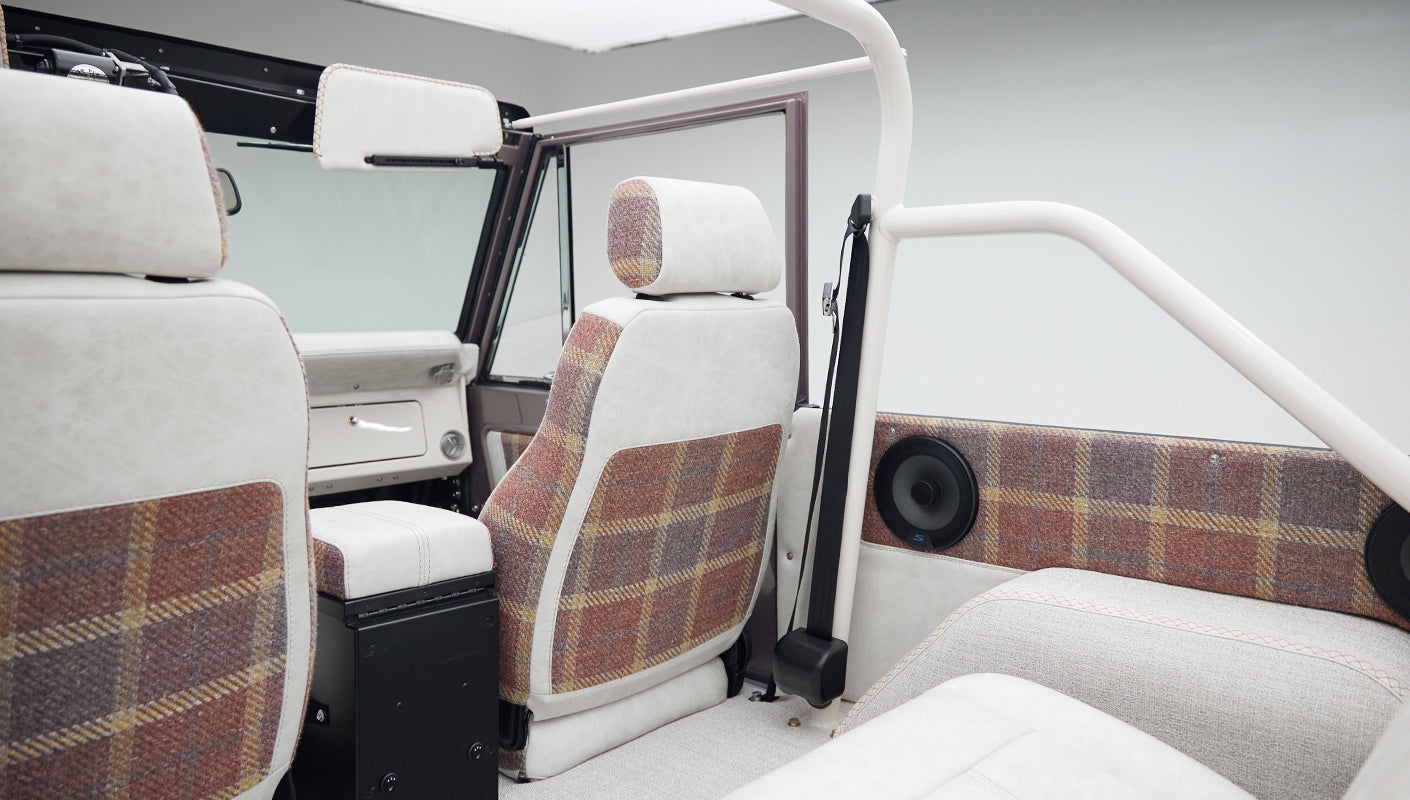 Interior view of Classic Ford Bronco seats with white and plaid upholstery and a roll cage