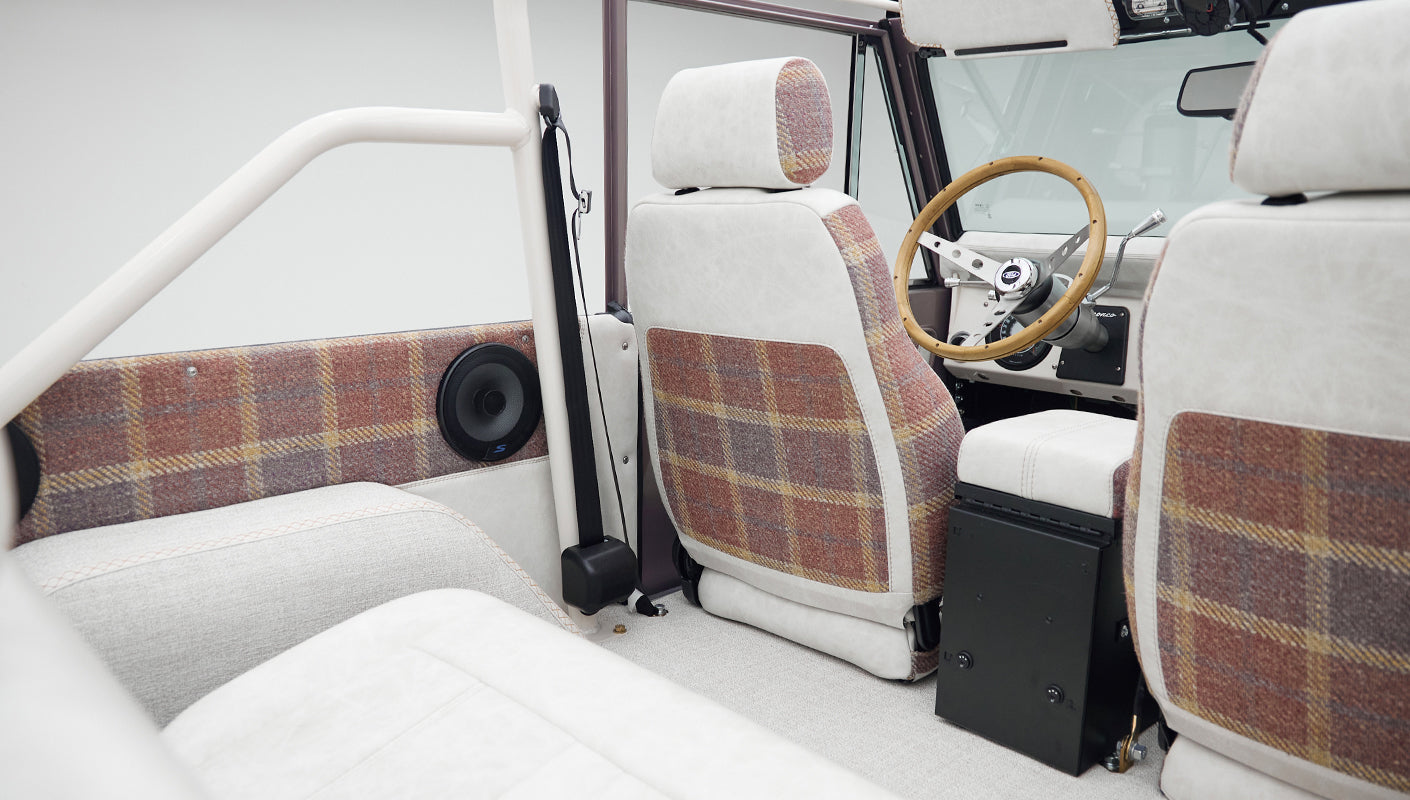 Classic Ford Bronco interior showing plaid and white seats with a roll cage and speakers