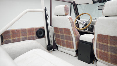 Classic Ford Bronco interior showing plaid and white seats with a roll cage and speakers
