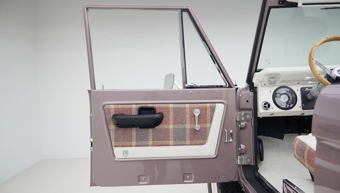 Open driver-side door of Classic Ford Bronco showing plaid and white door panel with black handle