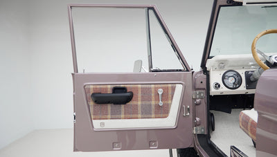 Open driver-side door of Classic Ford Bronco showing plaid and white door panel with black handle