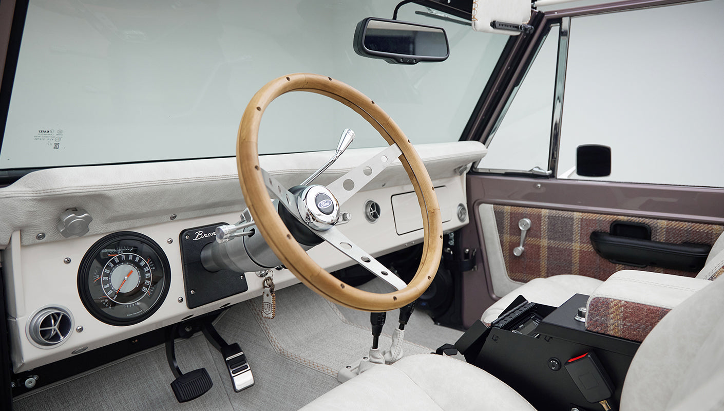 Classic Ford Bronco dashboard featuring wood steering wheel, speedometer, and air vents
