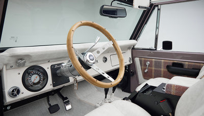 Classic Ford Bronco dashboard featuring wood steering wheel, speedometer, and air vents