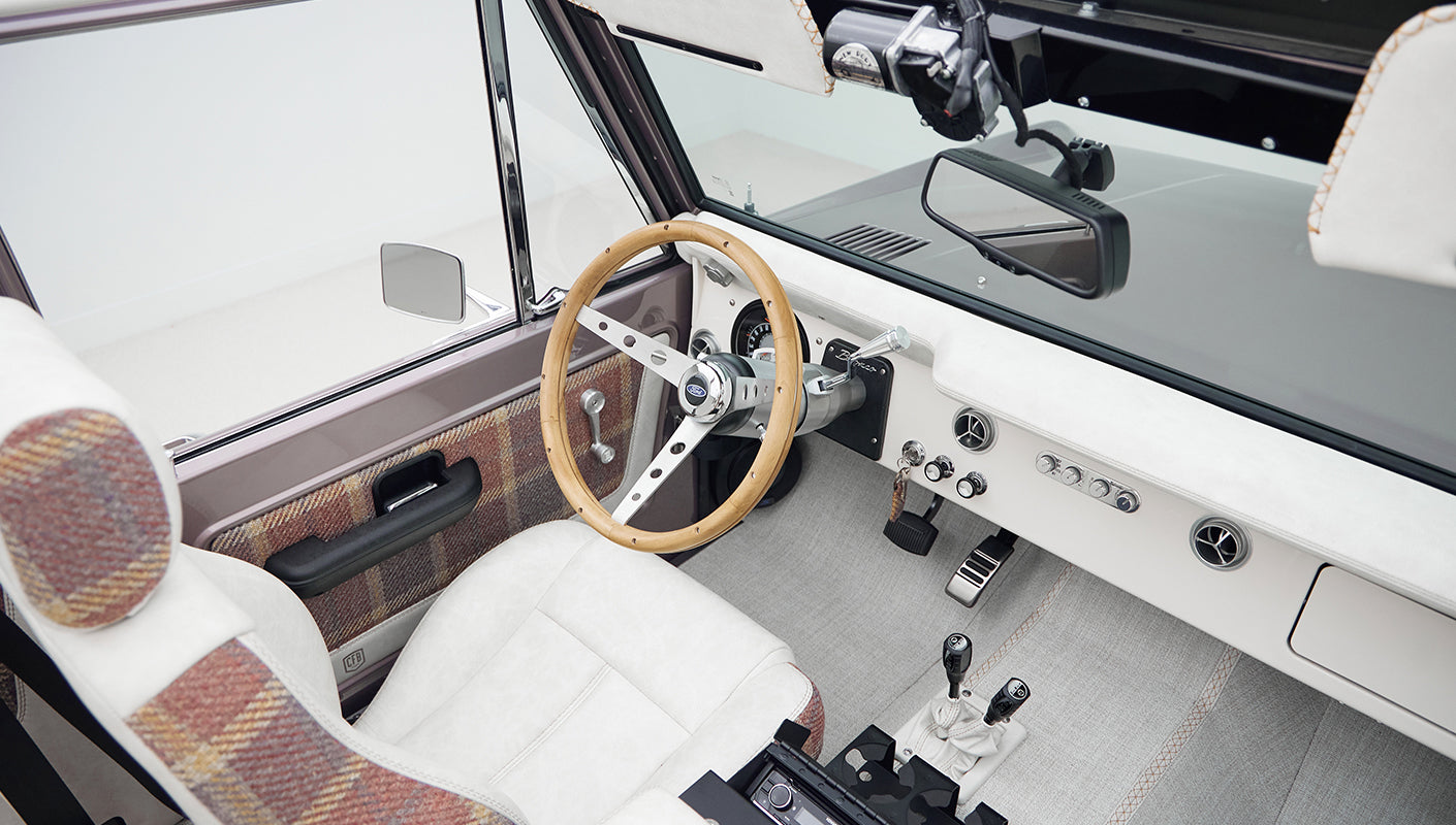 Front interior of Classic Ford Bronco showing steering wheel, instrument cluster, and plaid-accented upholstery