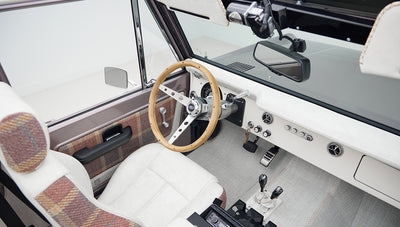 Front interior of Classic Ford Bronco showing steering wheel, instrument cluster, and plaid-accented upholstery