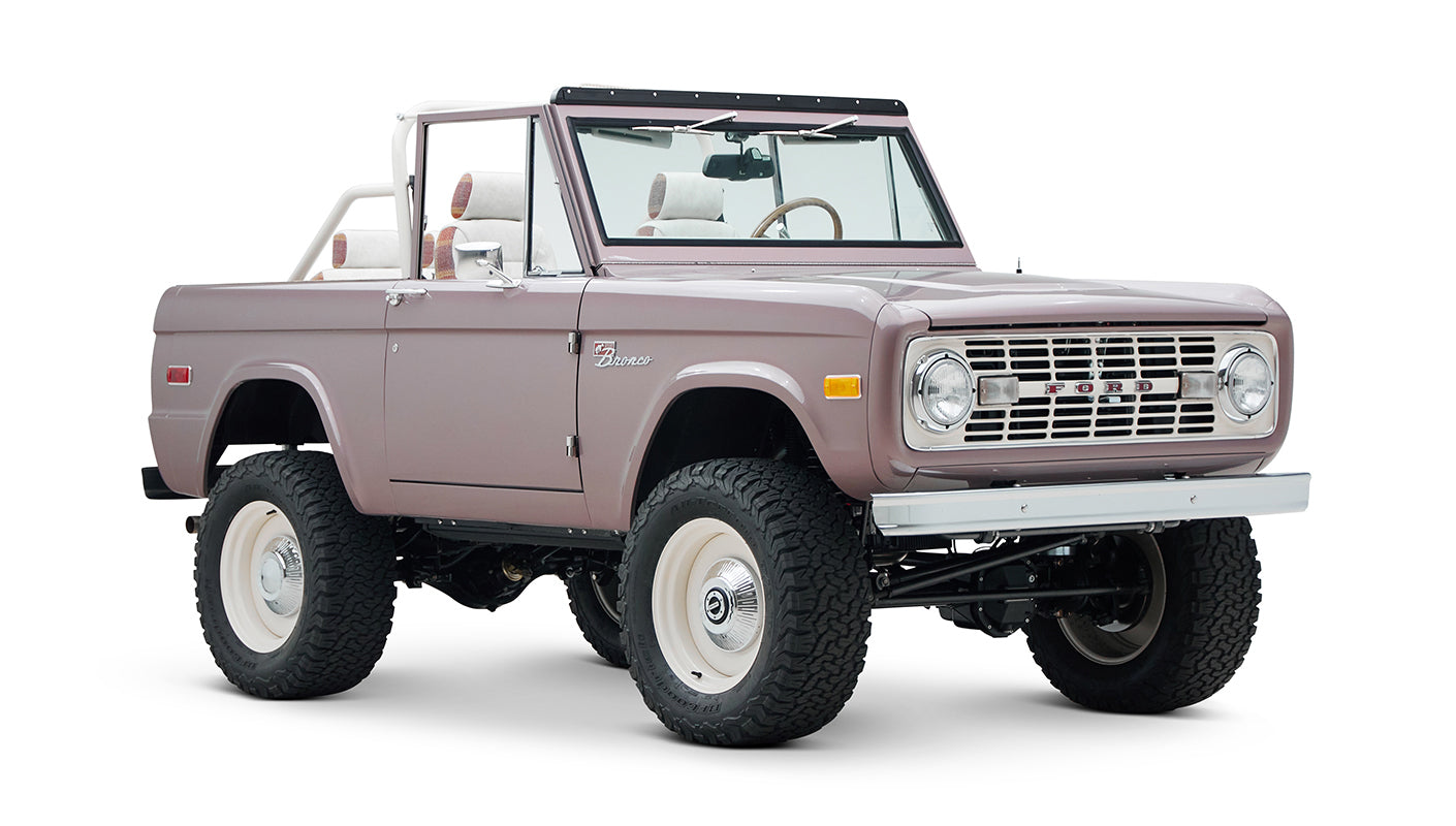 Side front view of soft pink Classic Ford Bronco with lifted suspension and white wheels on a white background