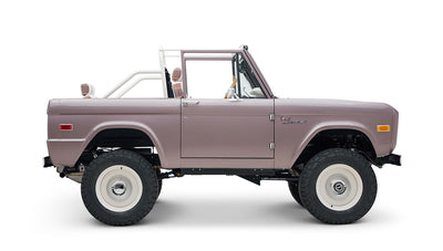 Classic Ford Bronco in soft pink with white wheels and lifted suspension, viewed from left side on white background