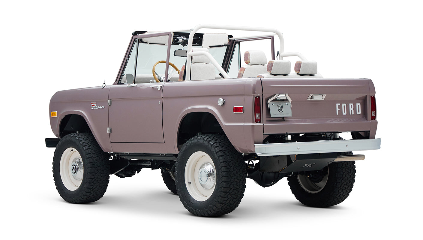 Rear view of soft pink Classic Ford Bronco with white wheels and lifted suspension on a white background