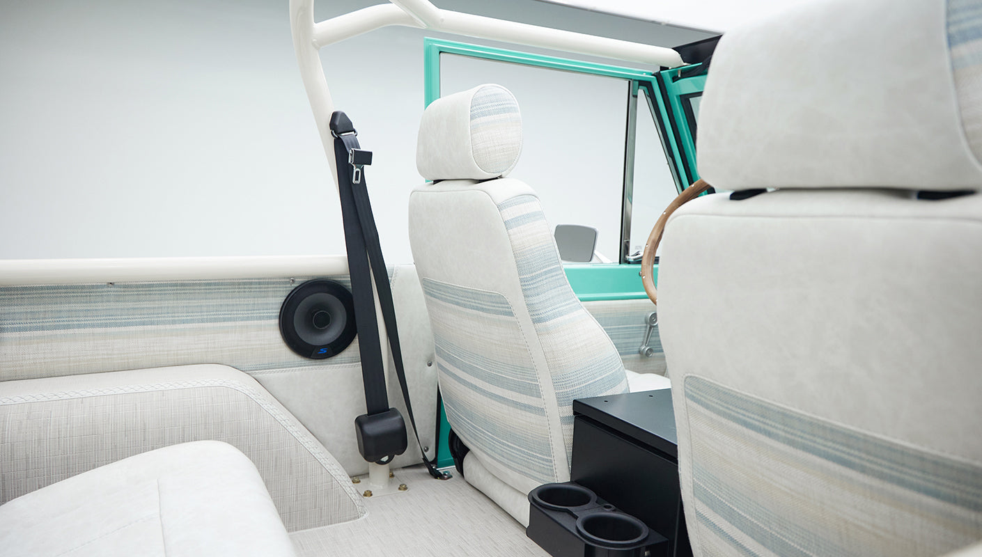 Close-up of rear seat headrests and roll cage bars inside a Classic Ford Bronco with white interior upholstery