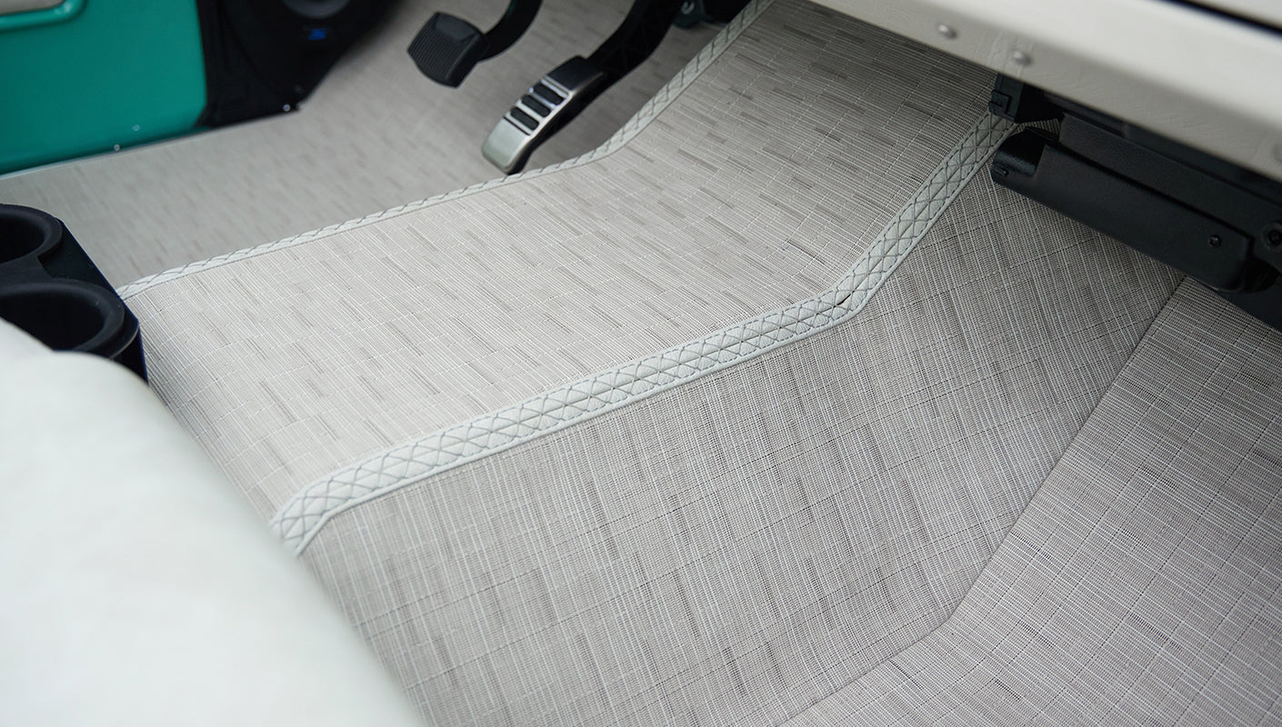 Floor area beneath steering wheel with cream textured floor mat and black pedals in Classic Ford Bronco