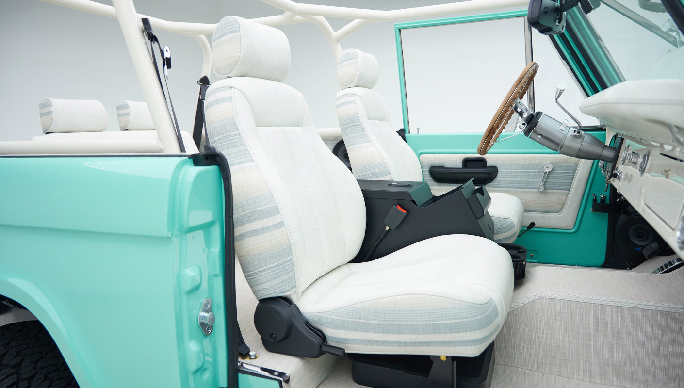 Interior of mint green Classic Ford Bronco showing front seats and dashboard with door open