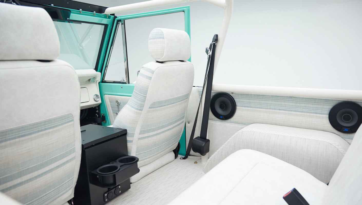 Interior view of classic Ford Bronco showing front and rear seats with white and light blue fabric