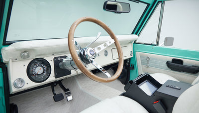 Driver side interior of Classic Ford Bronco with wood steering wheel and white dashboard
