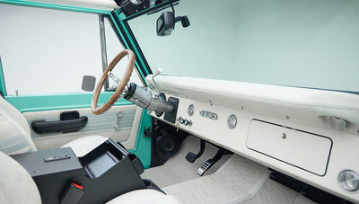 Interior dashboard view of Classic Ford Bronco with white upholstery and wood steering wheel