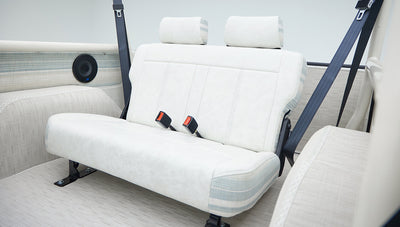 Rear bench seat of Classic Ford Bronco with white upholstery and striped fabric accents, along with seat belts