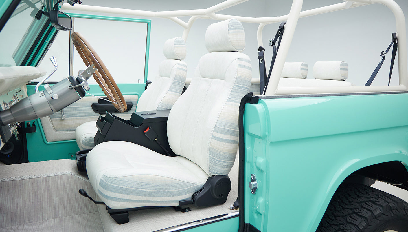 Interior of mint green Classic Ford Bronco showing white and blue striped seats and white roll bar
