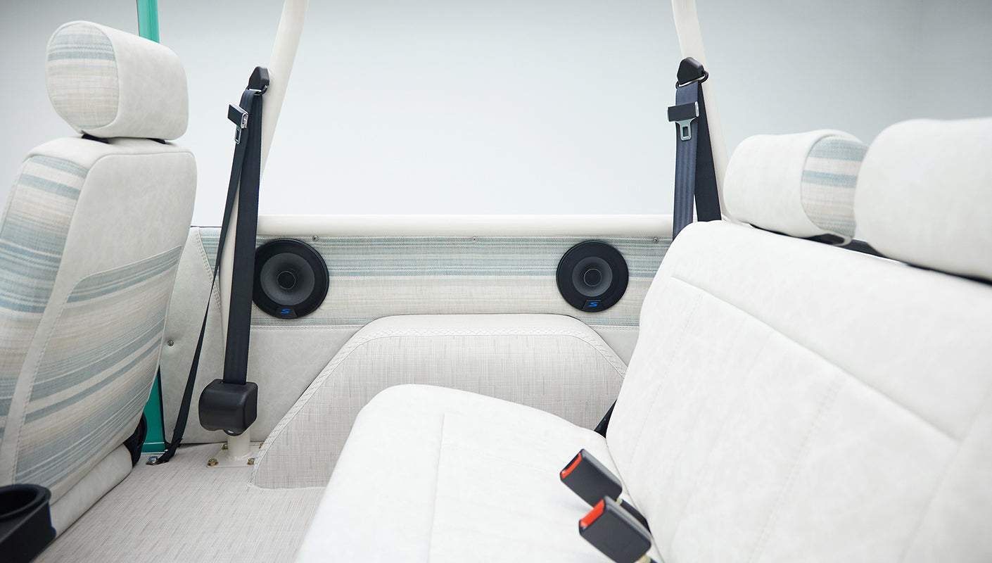Rear seating area side view showing white upholstery, striped fabric accents, with speakers and seat belt in Classic Ford