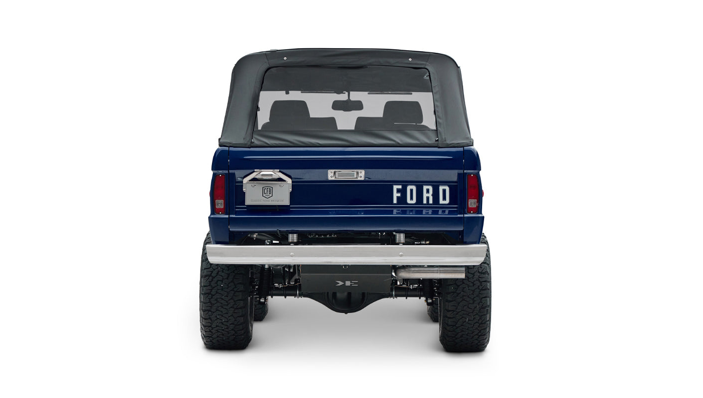 Classic Ford Bronco in sapphire blue with black soft top and lifted tires, rear view showing tailgate and bumper