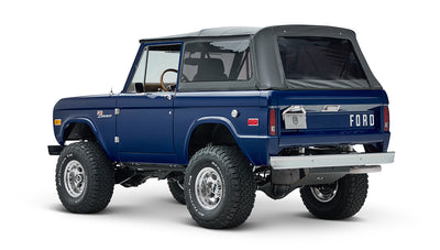 Classic Ford Bronco in sapphire blue with black soft top and lifted tires, rear side view