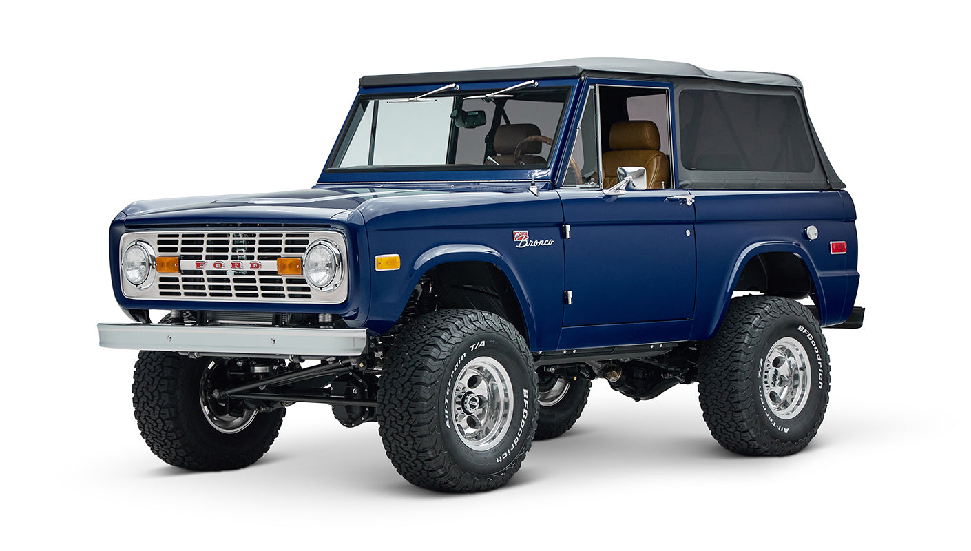 Front side view of blue Classic Ford Bronco with soft top and lifted suspension on white background