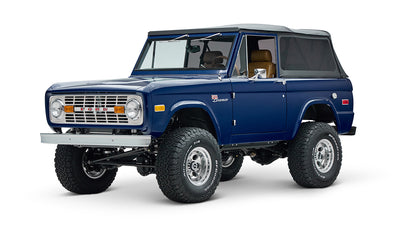 Front side view of blue Classic Ford Bronco with soft top and lifted suspension on white background