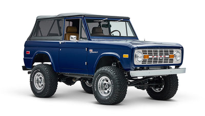 Blue Classic Ford Bronco with soft top, lifted suspension, and off-road tires on white background