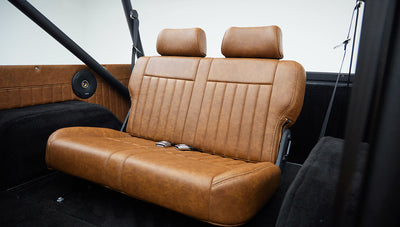 Tan leather rear bench seat inside classic Ford Bronco showing textured upholstery and seat belts