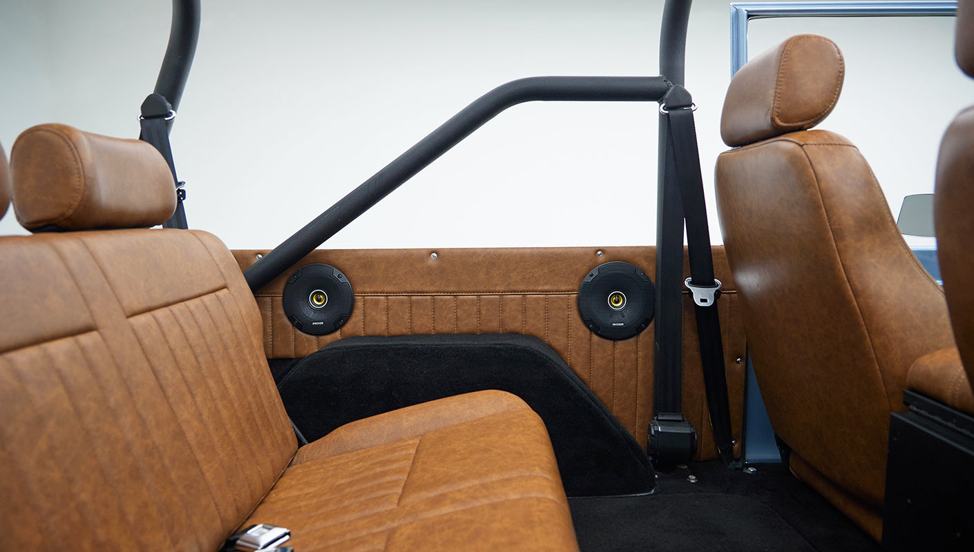 Tan leather rear seat and front seat with black seat belts and roll cage inside classic Ford Bronco
