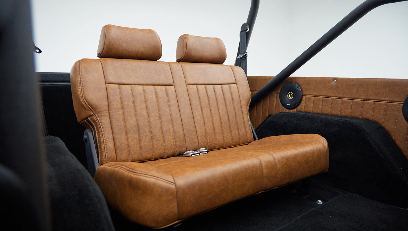 Tan leather rear seat with headrests and black roll cage bars inside classic Ford Bronco