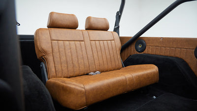 Tan leather rear seat with headrests and black roll cage bars inside classic Ford Bronco