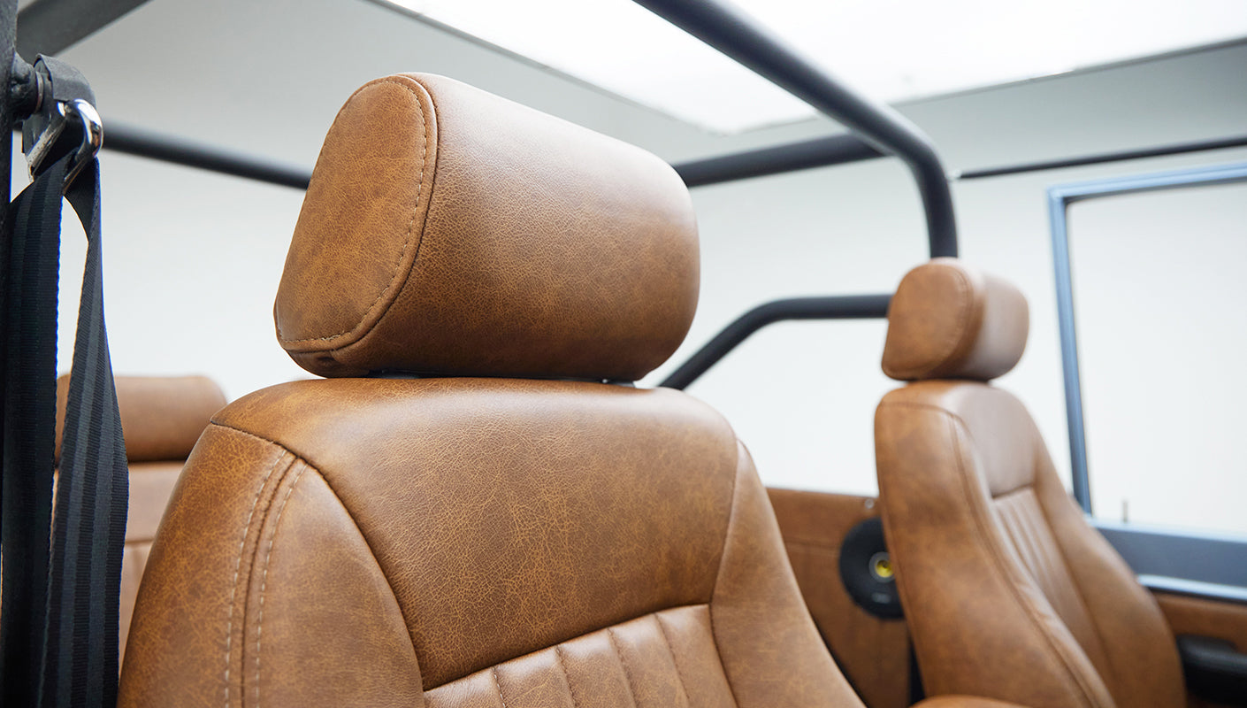 Close-up of tan leather headrest with front seats and black roll cage inside classic Ford Bronco