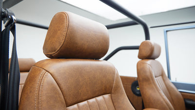 Close-up of tan leather headrest with front seats and black roll cage inside classic Ford Bronco