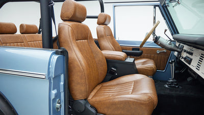 Open door view of tan leather front seats with center console and steering wheel inside classic Ford Bronco