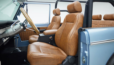 Side view of tan leather front seats with armrest, open door, and steering wheel inside classic Ford Bronco