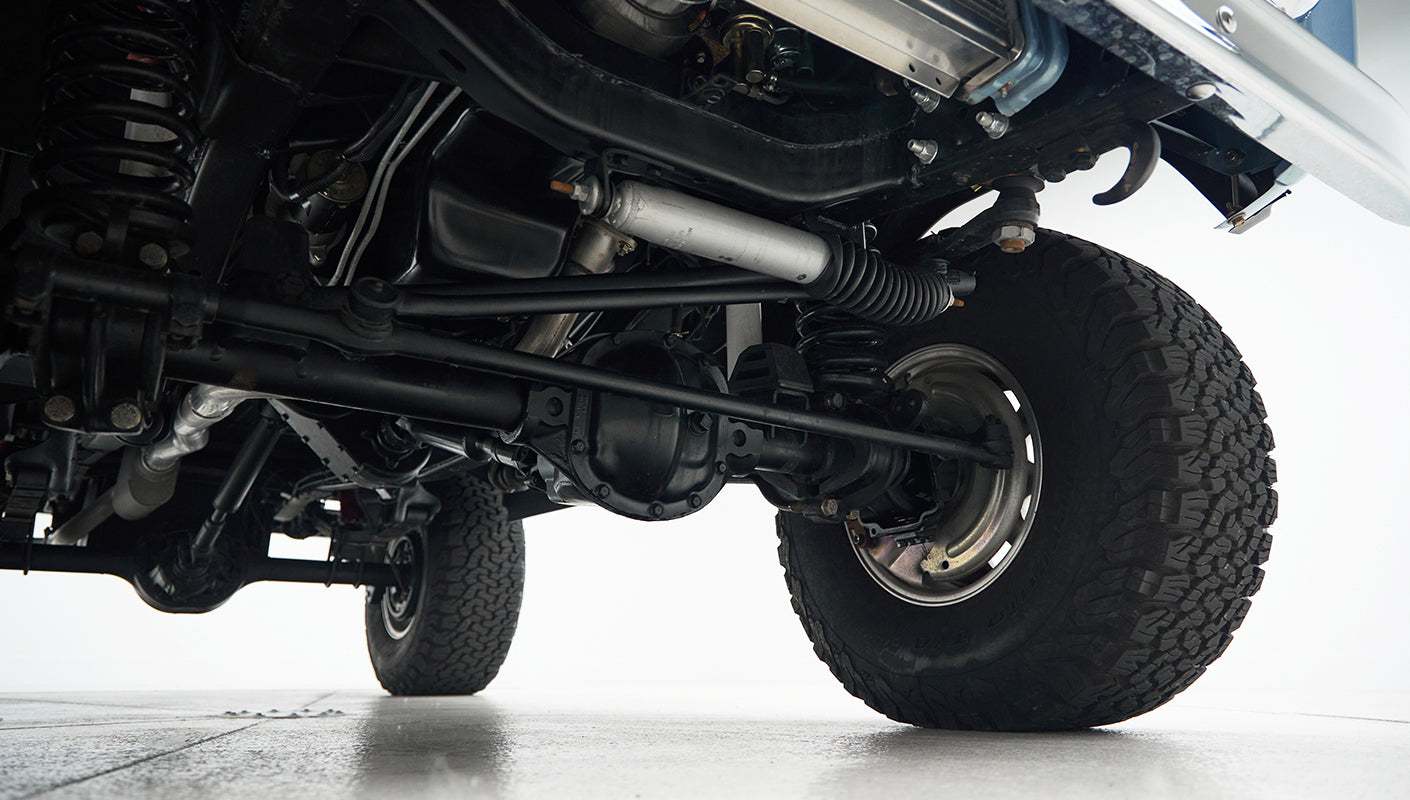 Undercarriage view showing suspension, axle, and large tire tread of classic Ford Bronco