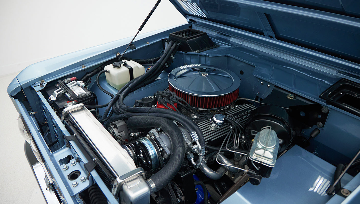 Angle view of engine bay in Classic Ford Bronco, Brittany Blue showing air filter, hoses, and cooling system