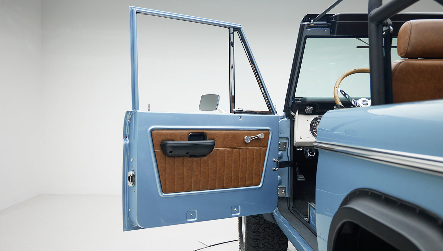 Open driver side door of Classic Ford Bronco showing blue painted door panel and brown interior
