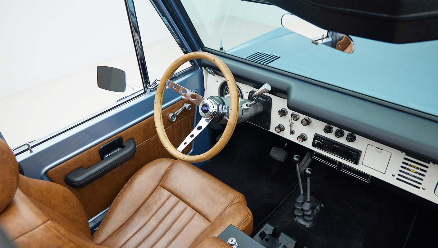 Interior view of Classic Ford Bronco showing steering wheel, dashboard, gear shifters, and seats